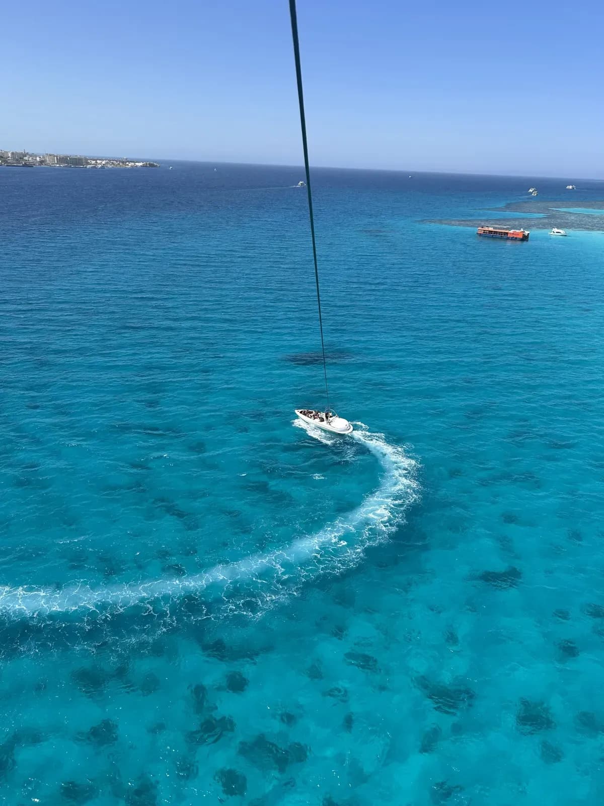 Le câble du parachute ascensionnel plonge vers le bateau, au-dessus d'une mer turquoise tachetée de coraux, au large de Hurghada