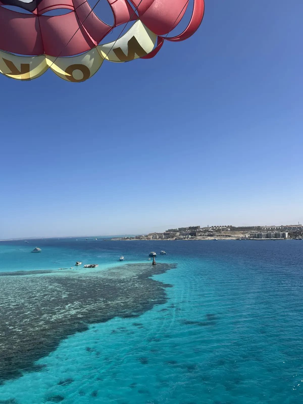 Voile rouge et jaune du parachute ascensionnel au-dessus d'un récif corallien et d'un lagon turquoise, face à la côte de Hurghada